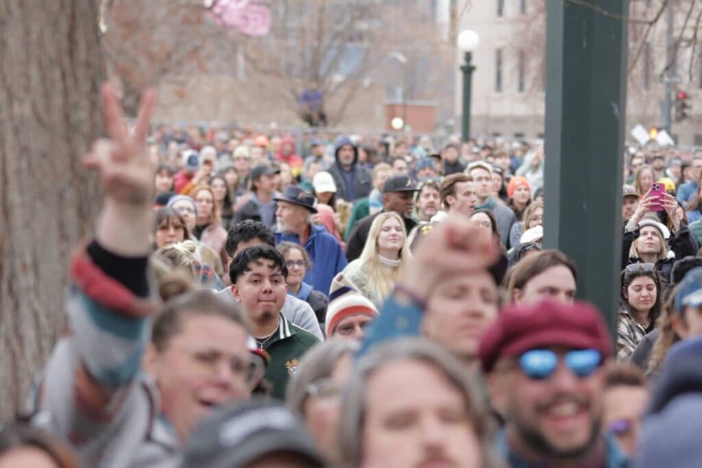 A large, diverse crowd of people watch a political rally.