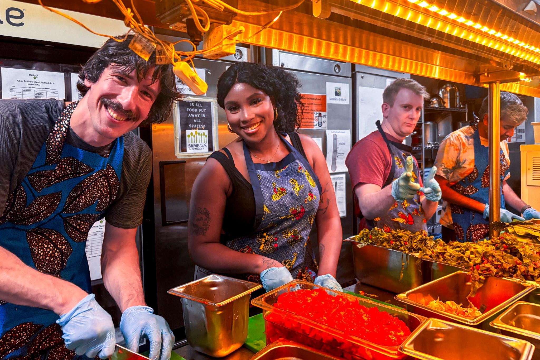 Four volunteers pose in front of vegetables and cutting boards in the SAME cafe kitchen, the night before chef Vasta Muhimpundu's menu takeover, Aug. 28, 2025.