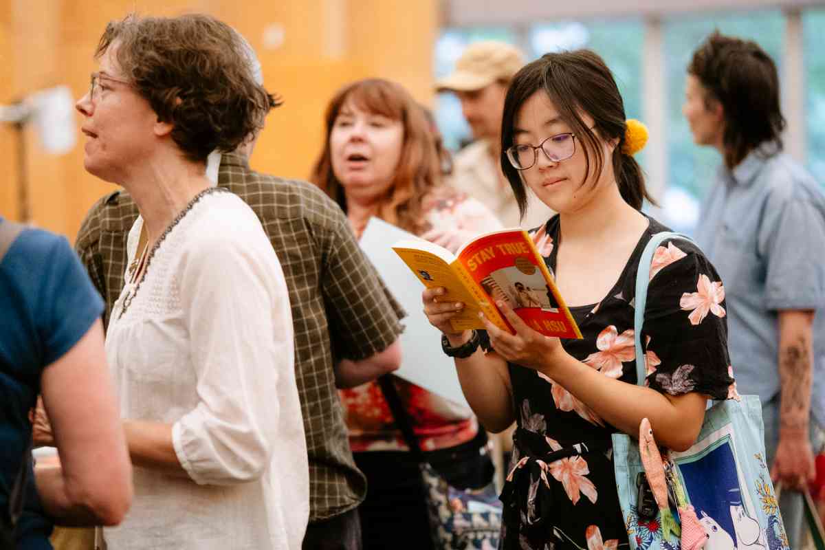 A crowd of people with one woman in a dress holding a book and reading from it